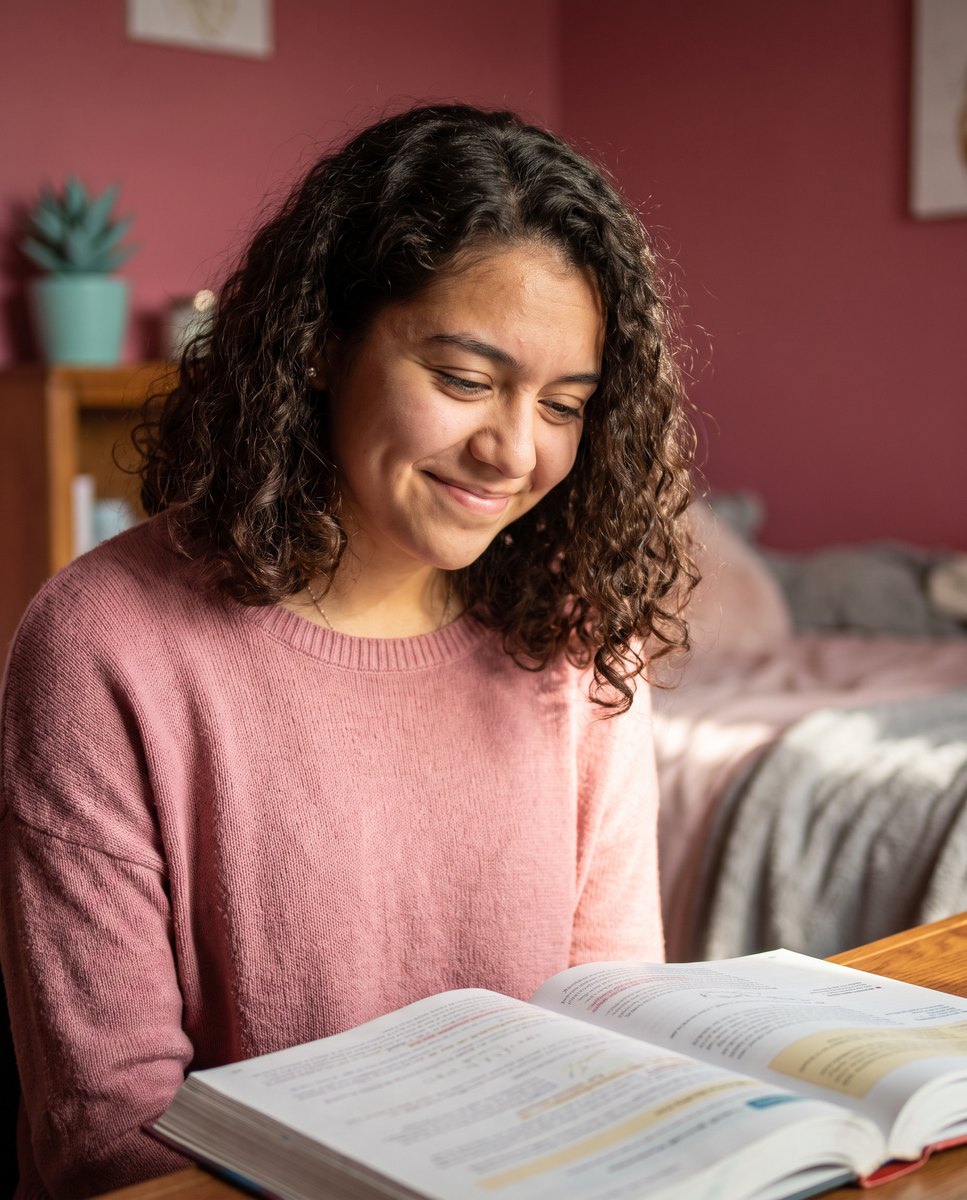 A high school student smiling as a concept clicks while reading a textbook at a desk.